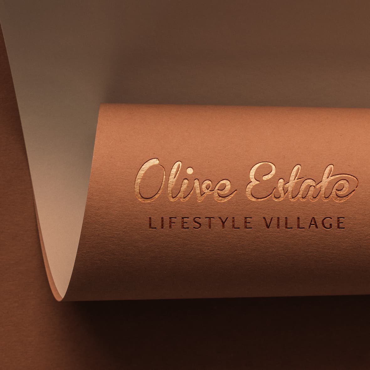 Close-up of olive estate lifestyle village embossed copper logo on warm brown paper, highlighting premium brand design.
