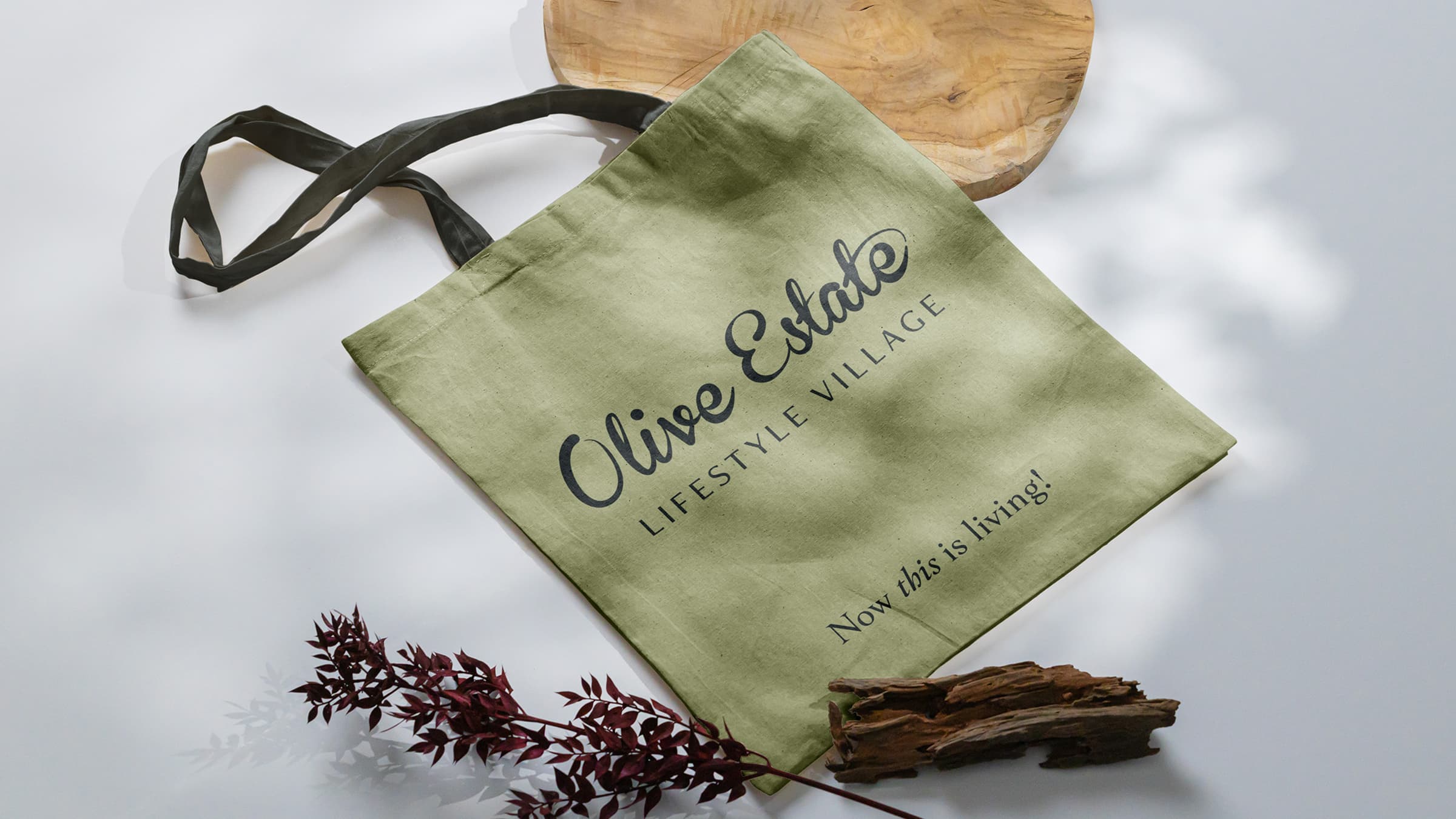 Branded olive estate lifestyle village tote bag with the slogan ‘now this is living! ’ placed on a bright white background.