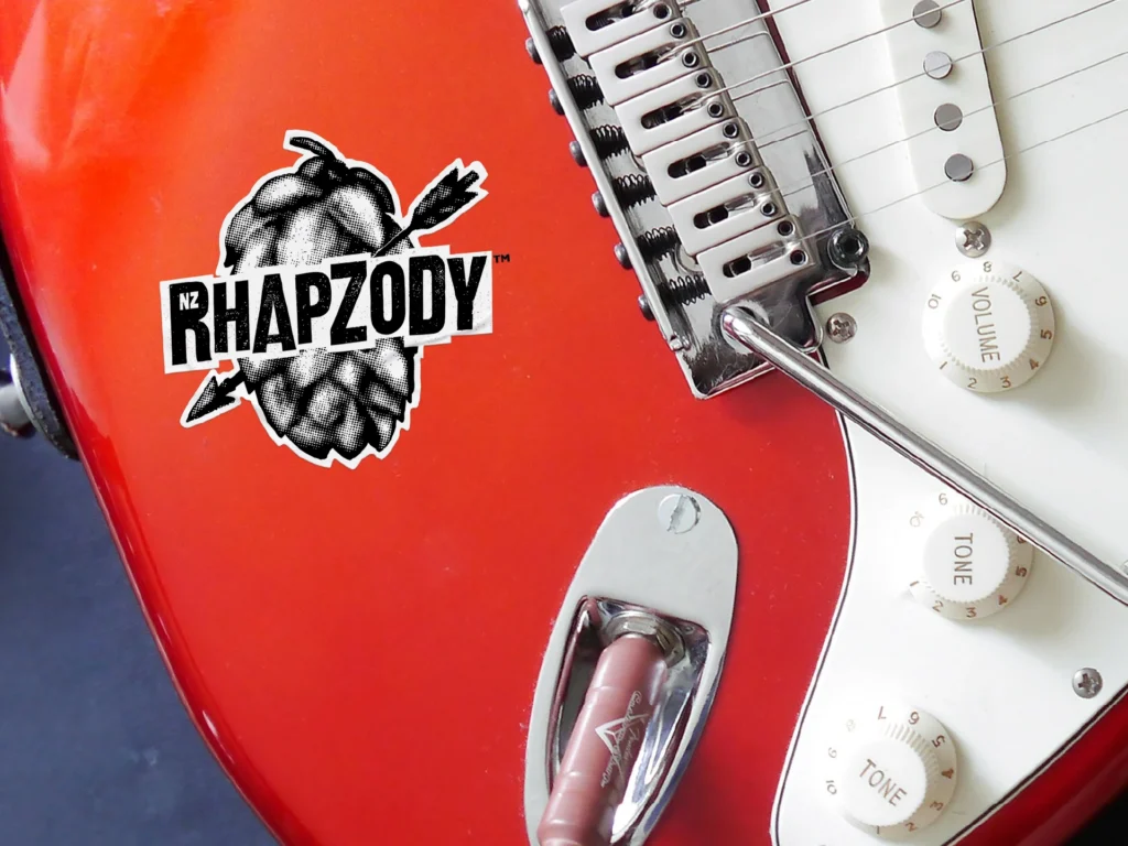 Closeup of a Rhapzody logo sticker placed on a red electric guitar body.