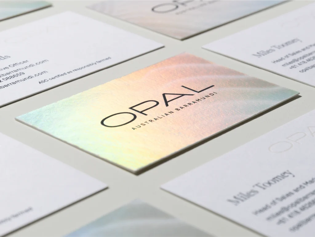 Multiple business cards with iridescent foil stamping displaying the Opal Australian Barramundi brand identity.