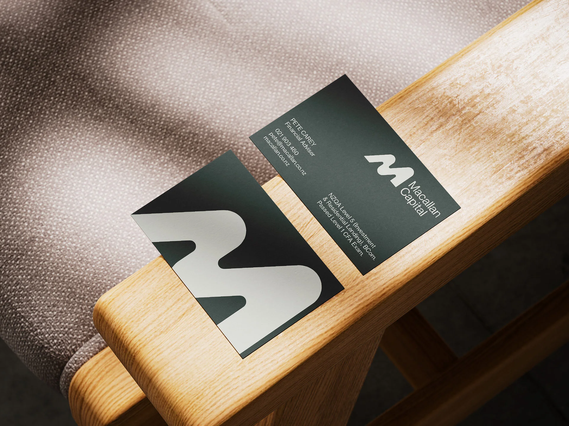 Premium dark green business cards with cream typography lying on a wooden armchair surface for Macallan Capital.