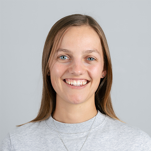Studio portrait of Emma, Creative at Downing, smiling with straight brown hair.
