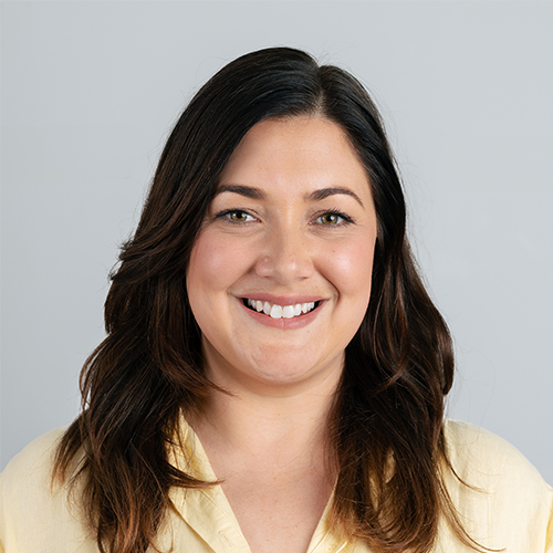 Studio portrait of Holly, Marketing Manager at Downing, smiling with long dark hair.