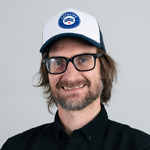 Studio portrait of Joseph, Creative Director at Downing, wearing glasses and a cap.