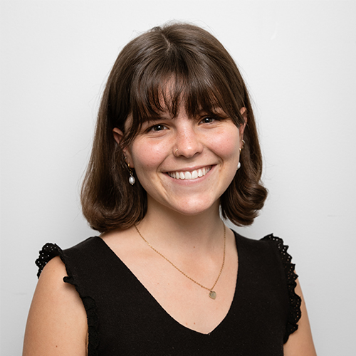 Studio portrait of Molly, Junior Creative at Downing, smiling with brown hair and bangs.