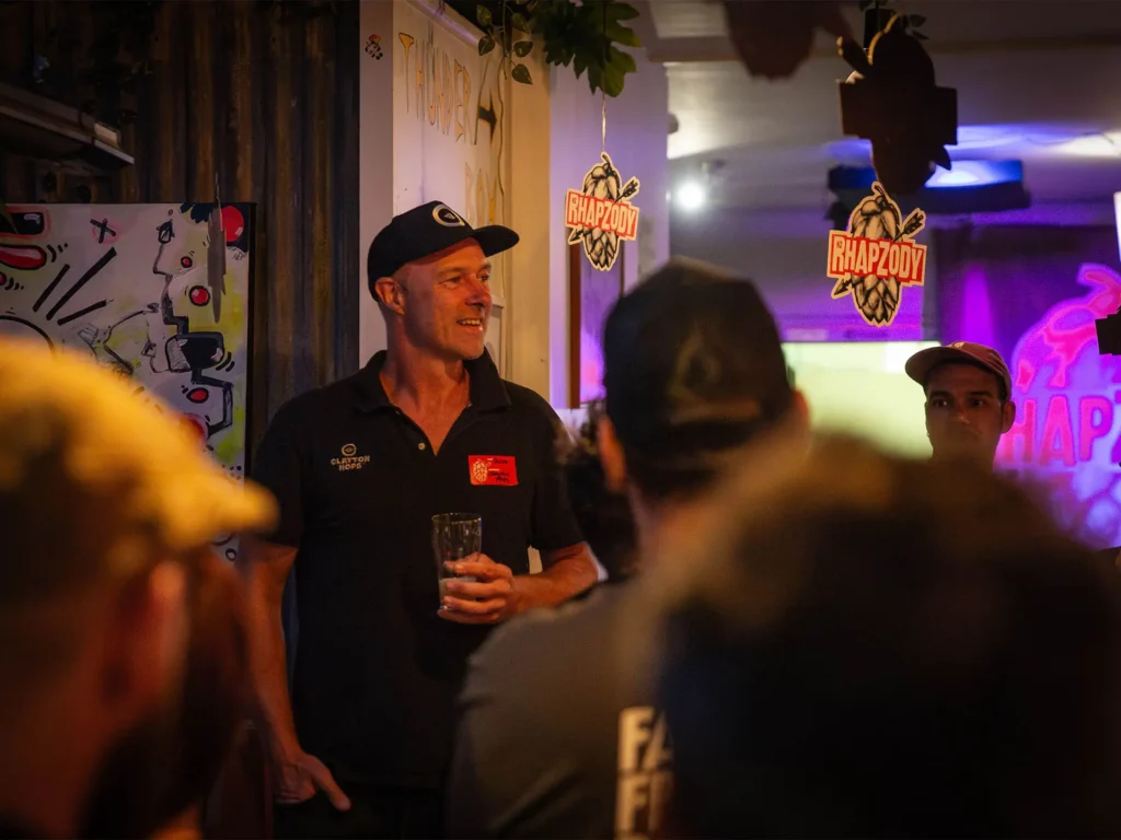 Man wearing a baseball cap smiling at an evening launch event for Clayton Hops' NZ Rhapzody brand release.