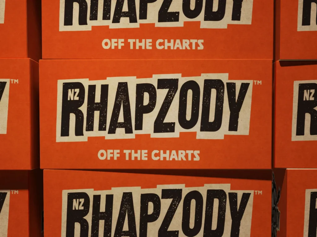 Stacked orange packaging boxes printed with bold black "NZ RHAPZODY - OFF THE CHARTS" typography for Clayton Hops