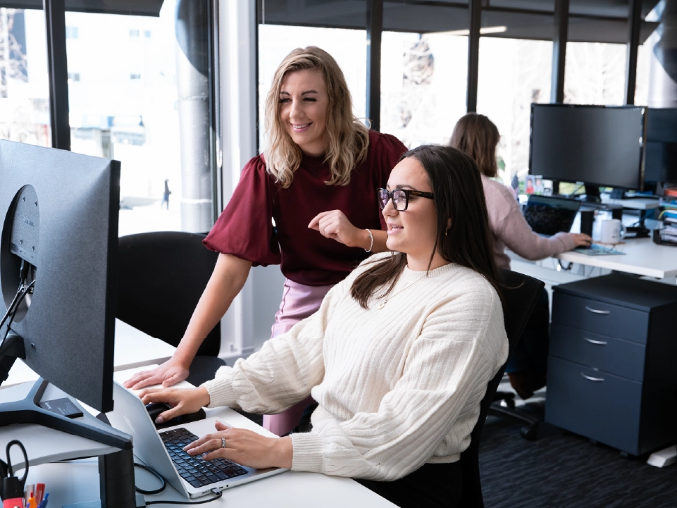 Sinead and Oriwa from the Downing team talking in an office environment alongside colleagues.