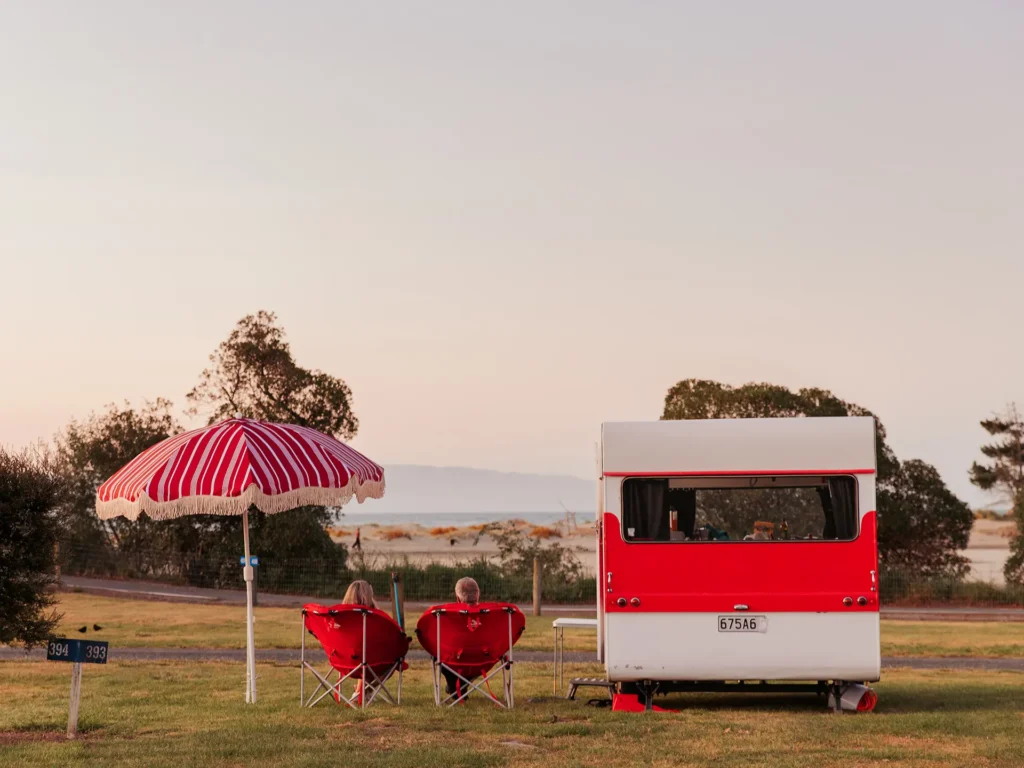 Couple relaxing by vintage caravan at Holiday park.